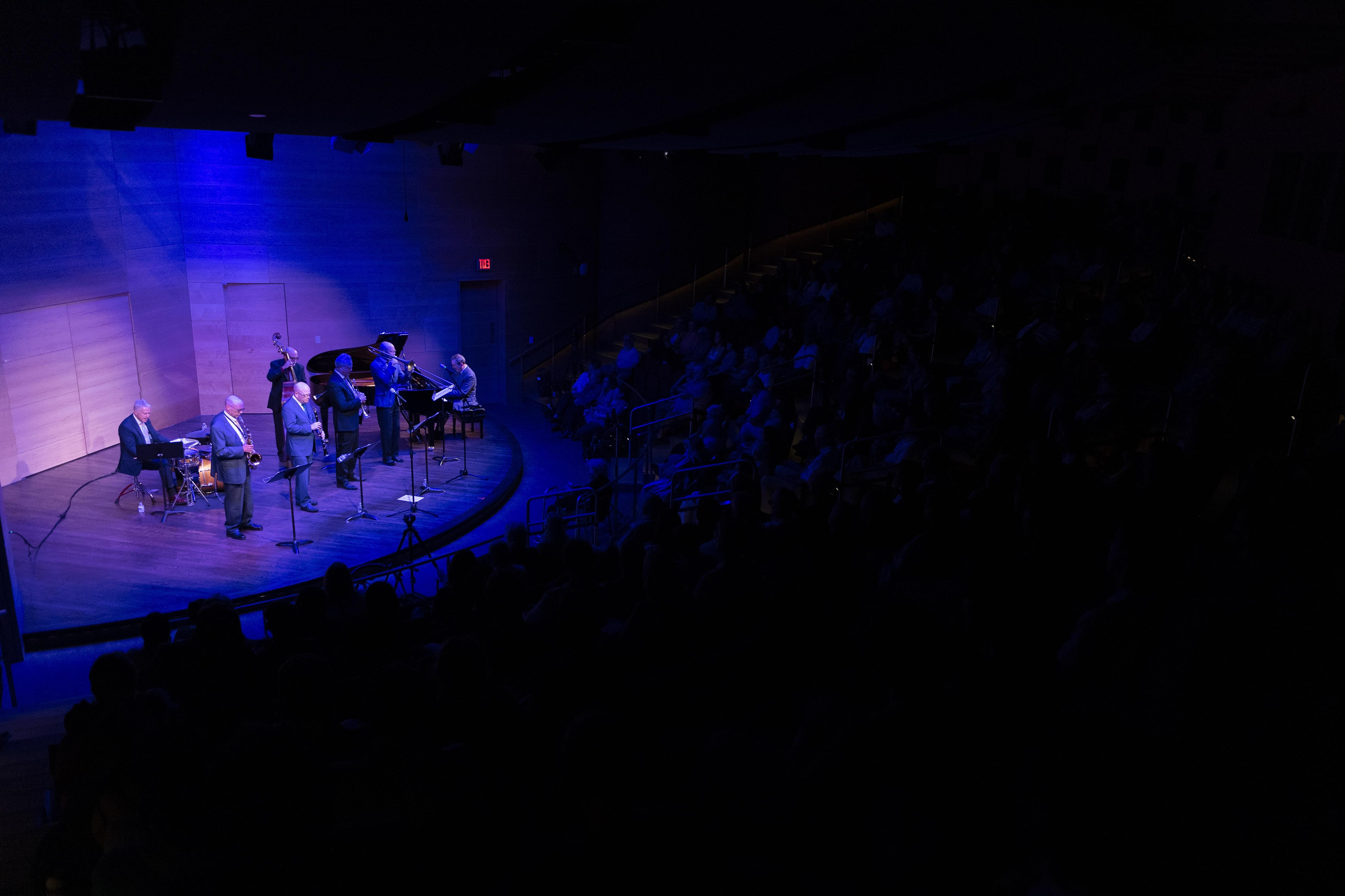 A packed Nunemaker Auditorium sits in darkness, listening to a jazz band on stage lit in soft blues.